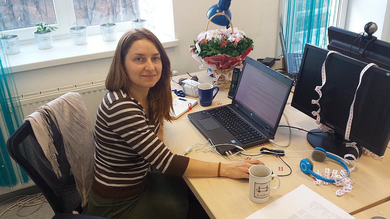 Halyna Shporlyuk sitzt an ihrem ersten Tag bei Conscensia an ihrem Schreibtisch, mit einer dänischen Flaggen-Tasse im Vordergrund und einem Willkommensstrauß, symbolisch für den warmen Empfang und den Beginn ihrer bedeutenden Reise.