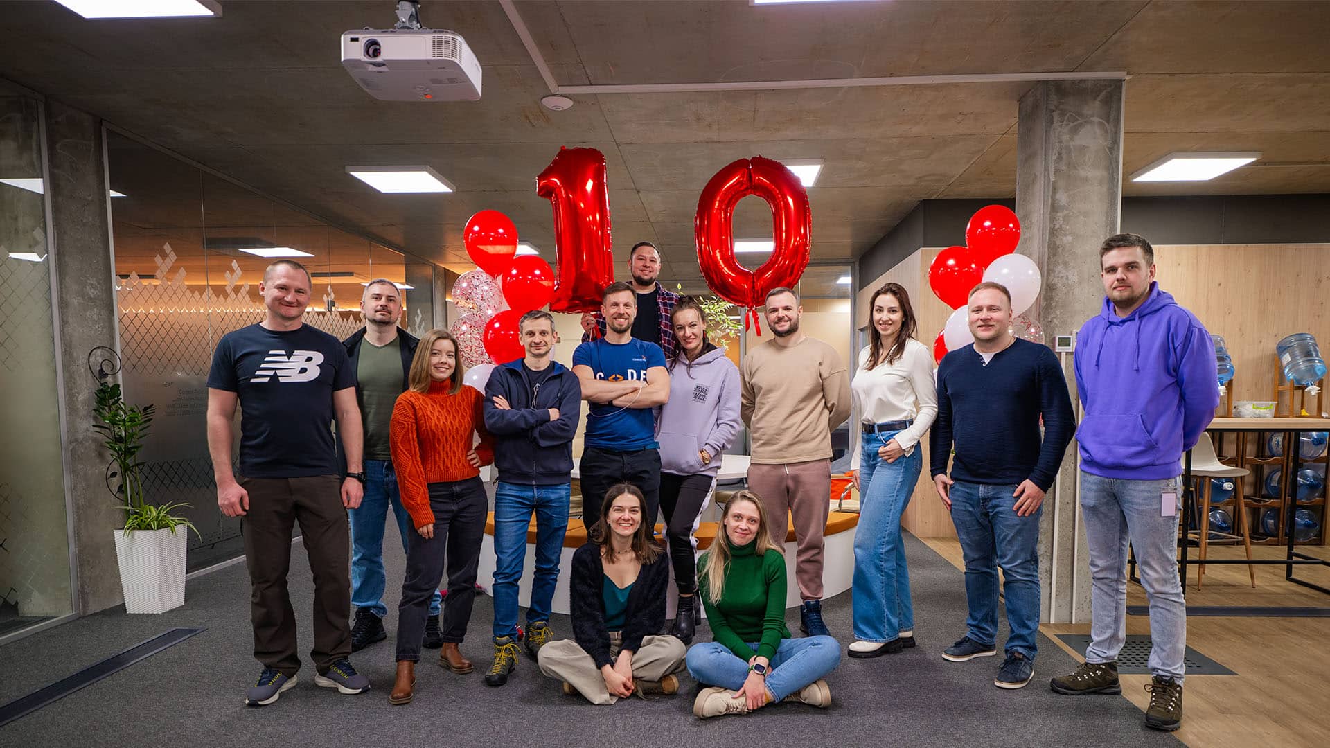 Gruppe von lächelnden Kollegen feiert 10 Jahre Partnerschaft mit roten Luftballons und '10' Folienballons in einem Büro in der Ukraine.