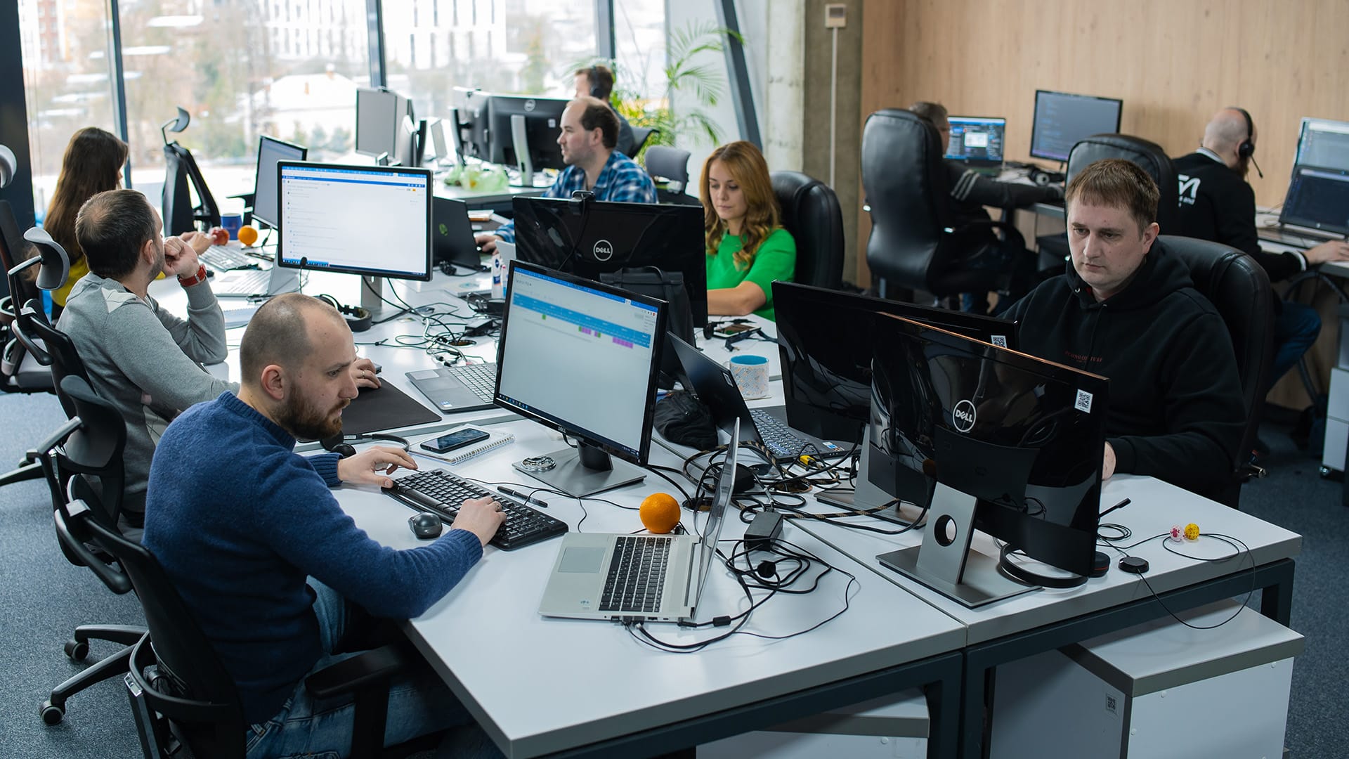 A group of software developers working intently at their desks in an open office setting with computers, monitors, and coding on screens.